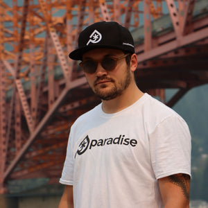 The Paradise Skis branded t-shirt in white. Young man wearing a white Paradise Skis t-shirt and a black hat